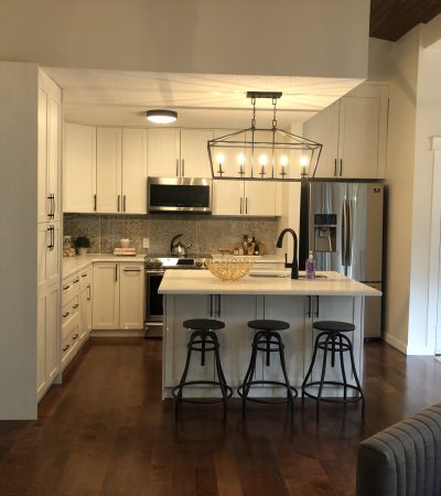 another angle of the Remodeled Island style kitchen with a beautiful chandelier. White cabinets with black chairs and warm yellow lighting